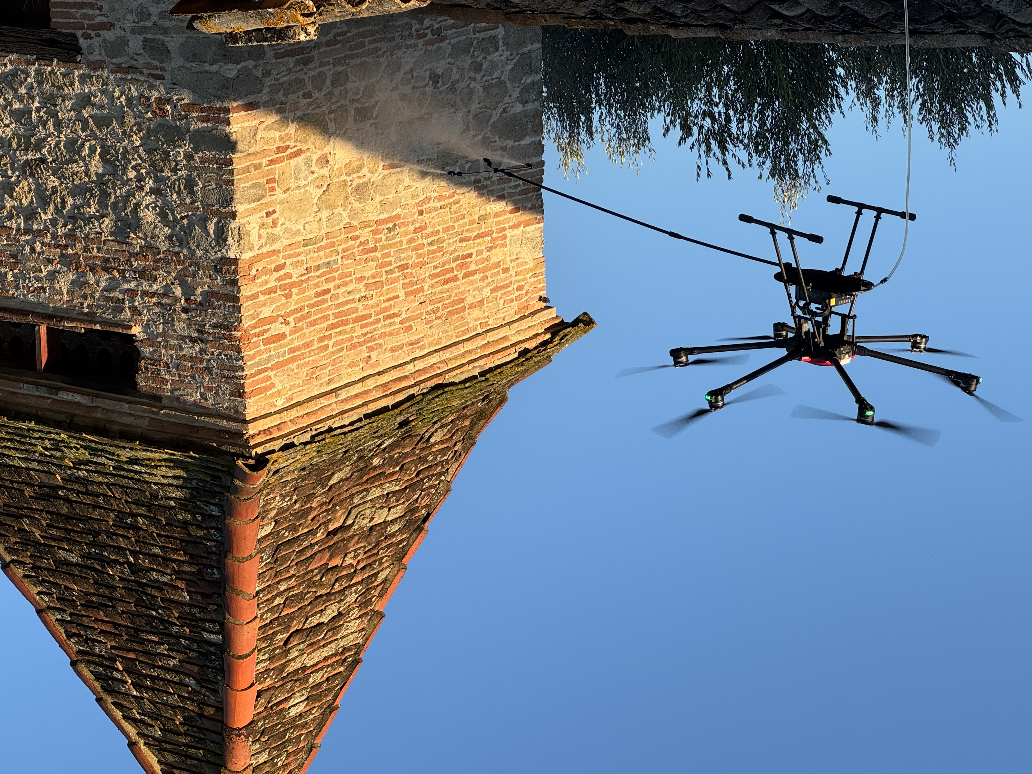 Drone en pulvérisation à proximité d’une façade en brique et pierre